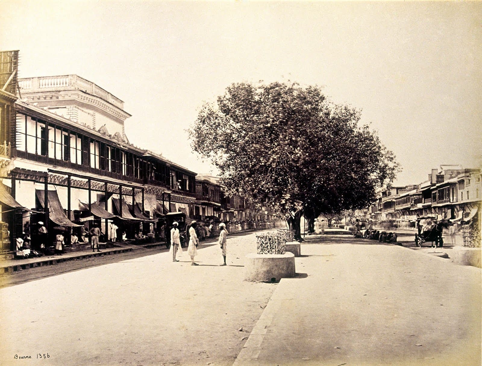 Samuel Bourne's 1860s photograph looking down Chandni Chowk, a broad tree-lined avenue crowded with people, with the channel line running up its centre.