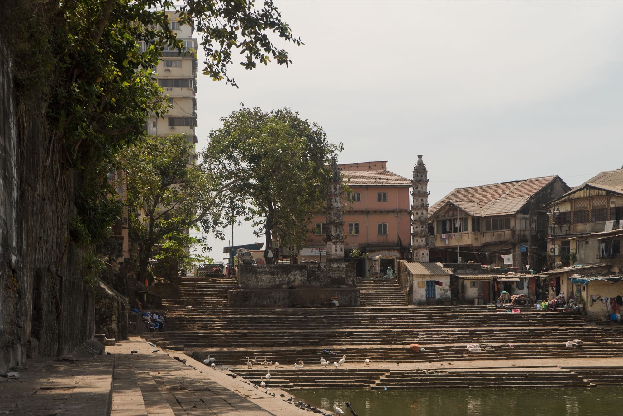 Banganga Tank at Walkeshwar: a rectangular stepped stone tank ringed by dense residential towers, with temple deepstambhas at the water's edge.