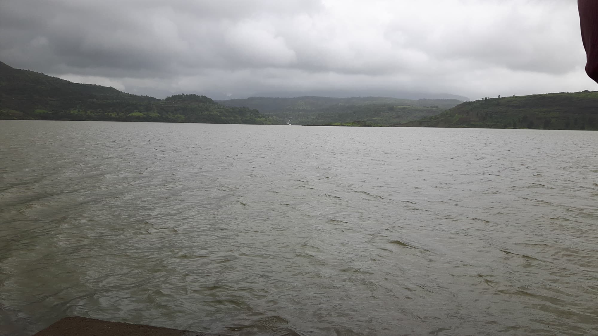 A dam on the Vaitarna river in full monsoon flow, water sheeting over the spillway between green Western Ghats hills.