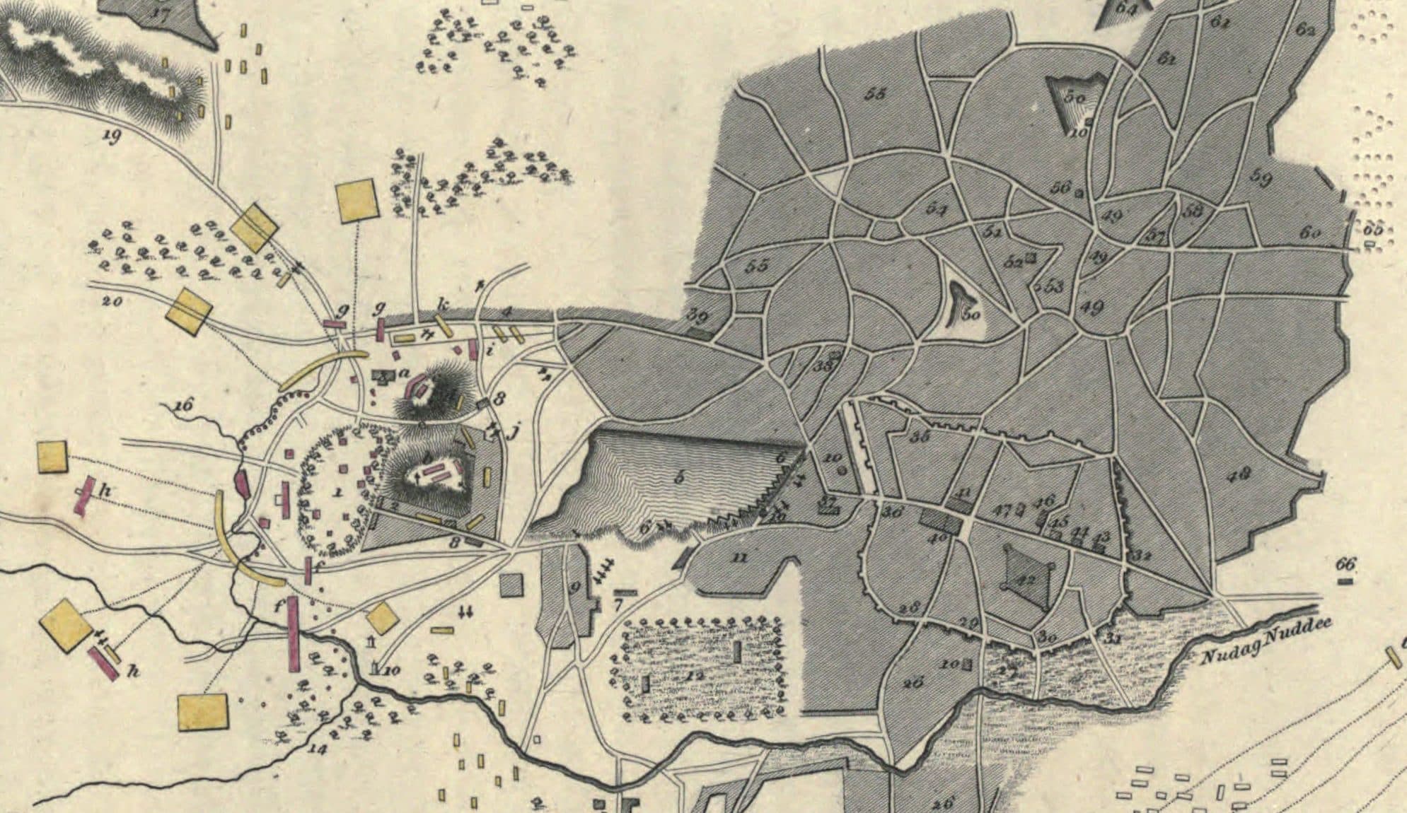 A detail of a hand-coloured engraved plan of Nagpur from 1819. The walled city, shaded grey and cut by a web of lanes, fills the right half. To its left a large hatched tank lies between the city and two small fortified hills, and a dark river line runs along the bottom of the city, its label ending 'Nuddee'. Roads, gardens and yellow and red marks for troop positions are scattered across the plain.