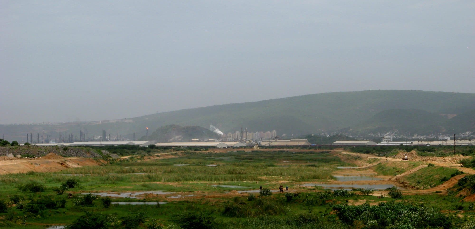 The Meghadri Gedda near Visakhapatnam airport in 2009: a wide, flat valley floor of green marsh and shallow pools, with hills and the city's buildings in the haze behind.