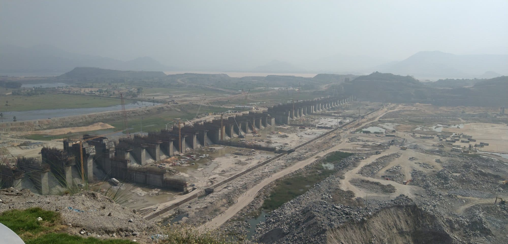 The Polavaram dam under construction on the Godavari in February 2019: a long line of concrete piers across a dry, excavated riverbed, with hills behind.